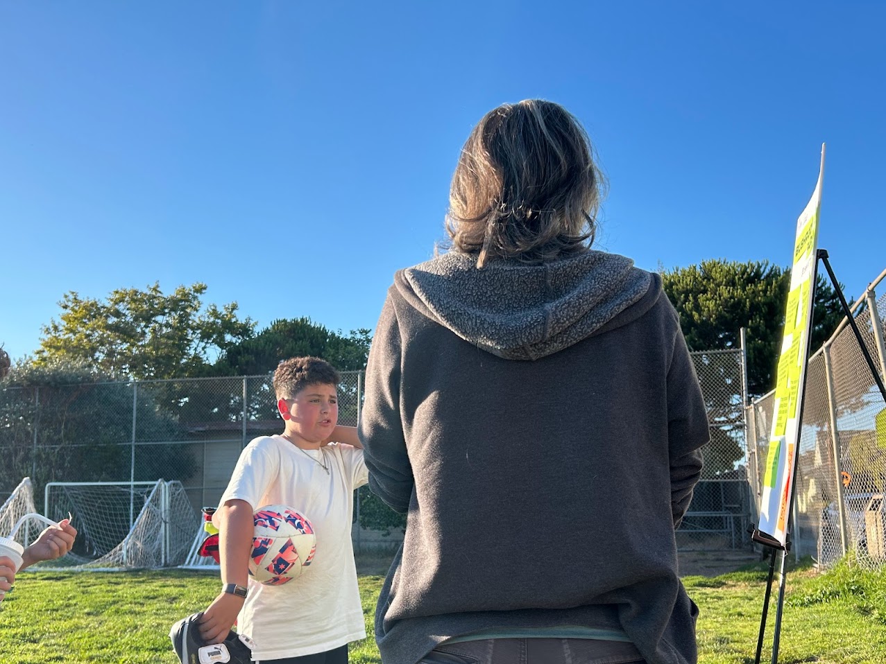 A neighbor speaking with a child about what they'd like to see in Bushrod Park. They are pointing at a sign with other suggestions.