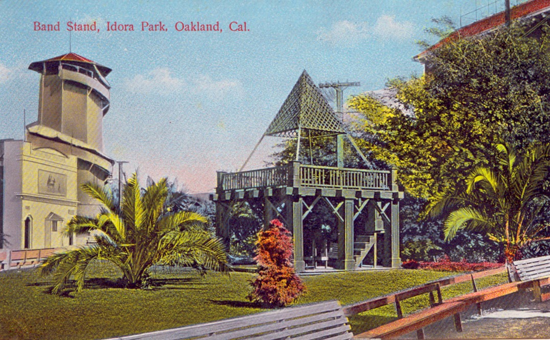 Postcard of Idora Park, featuring the the bandstand, benches, and a lush green lawn with low palms.