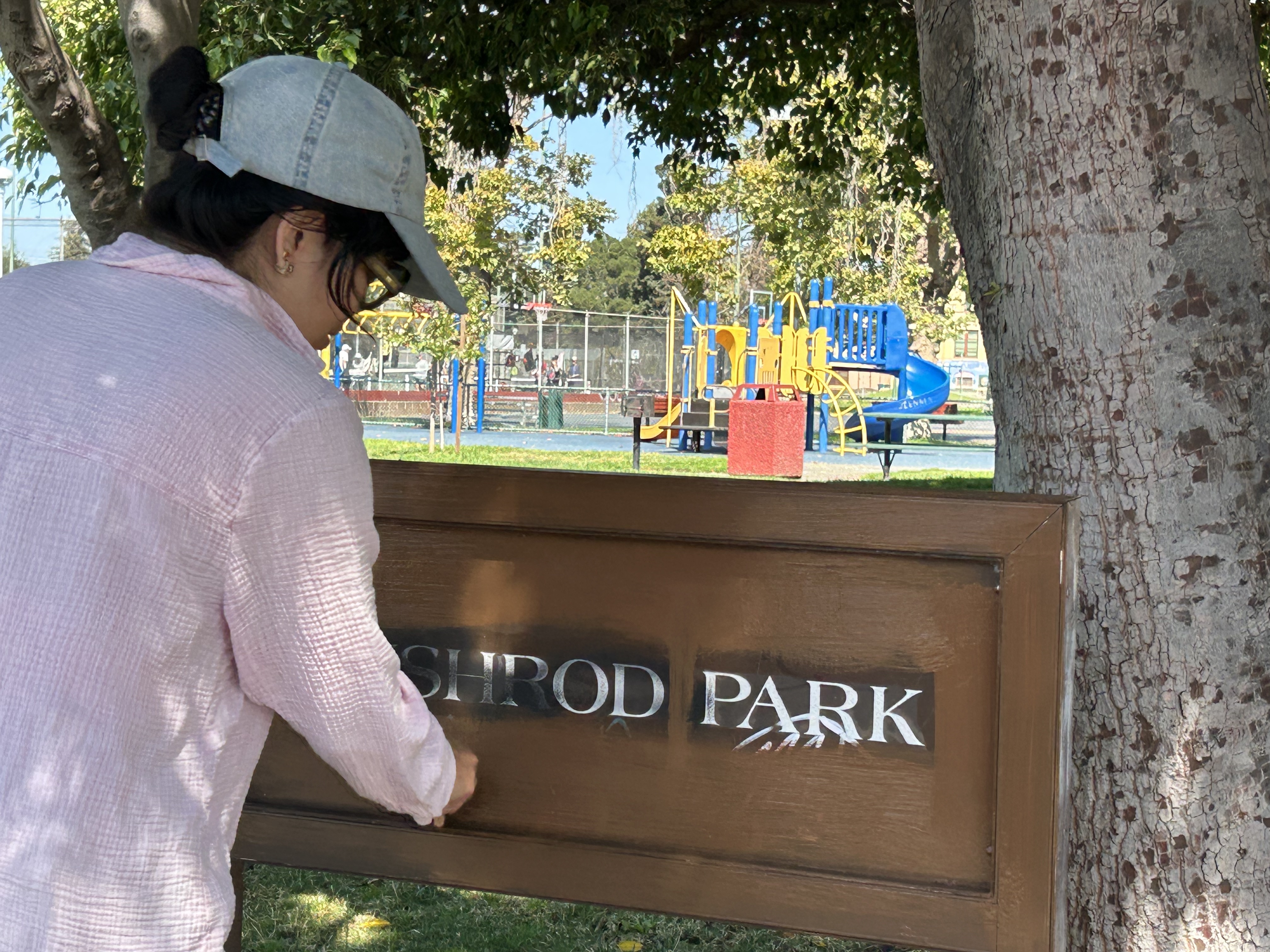 A person in a hat and glasses gives the Bushrod Park sign a fresh coat of paint, covering previous blemishes.